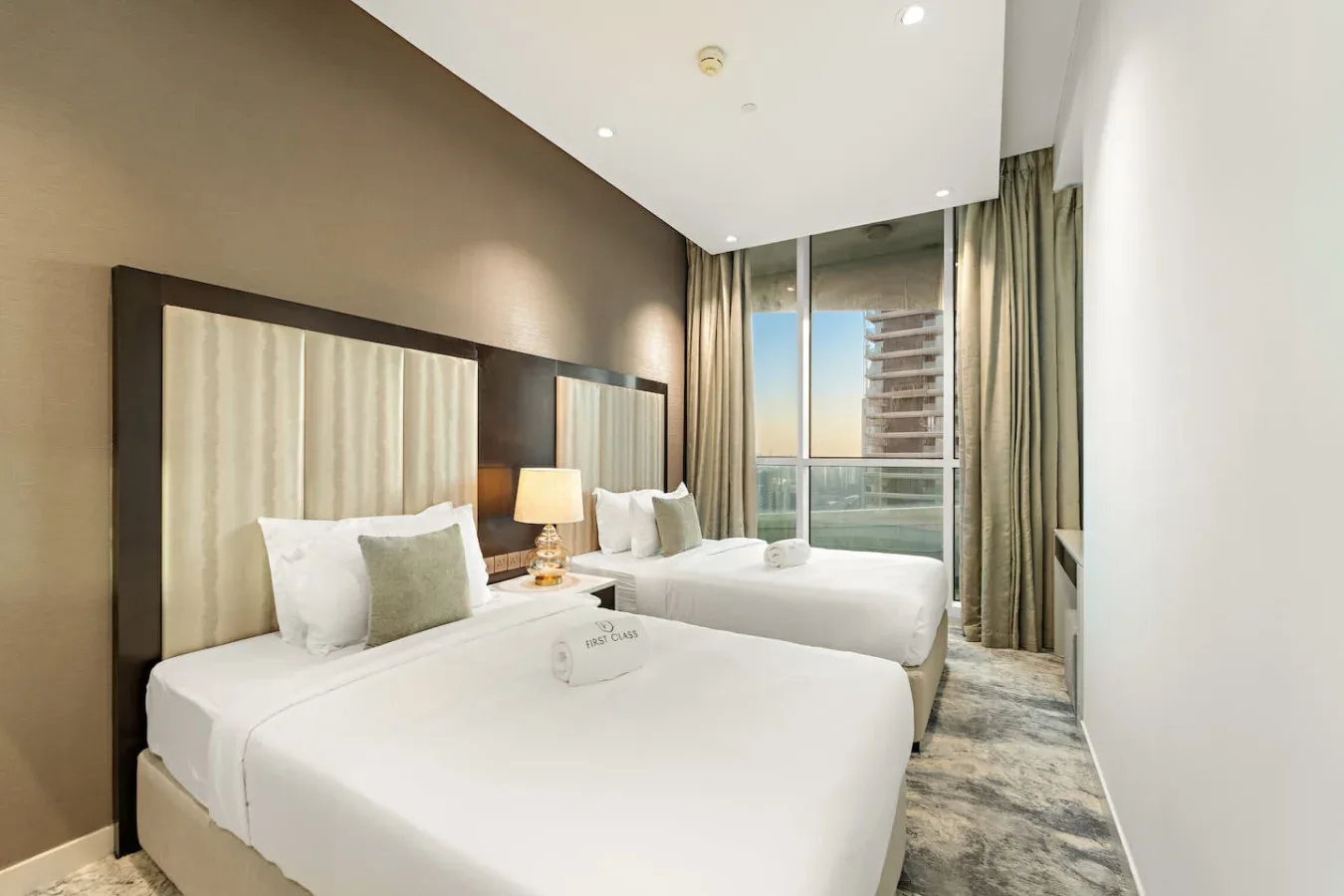 A bright bedroom with two beds, bedside lamps, and a large window.