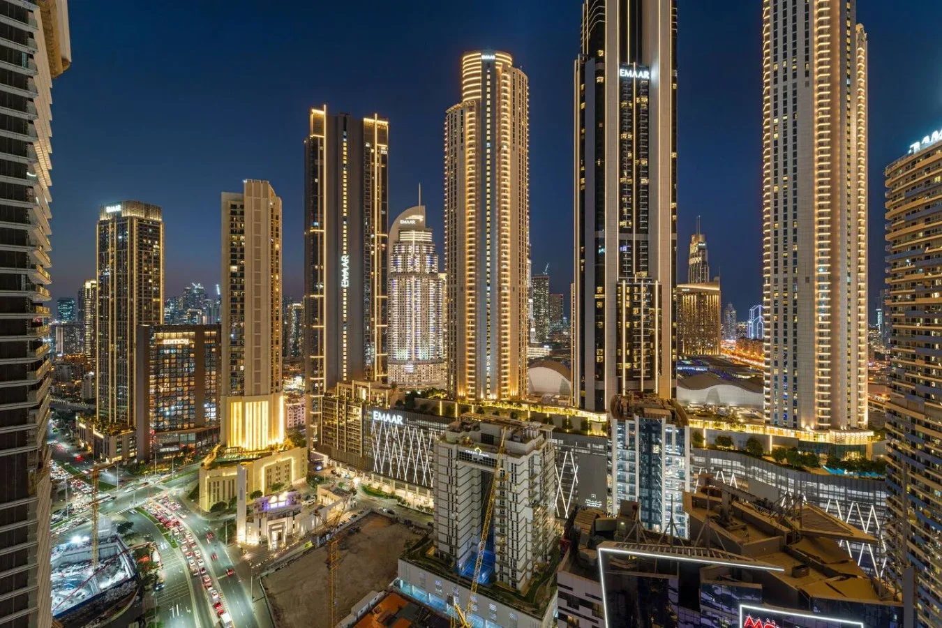 A nighttime city skyline with illuminated high-rise buildings and roads below.
