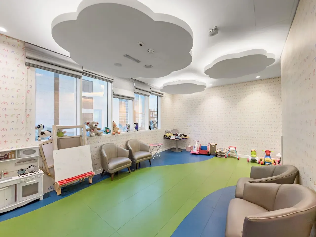 A bright children's playroom with colorful floor mats and seating by the windows.