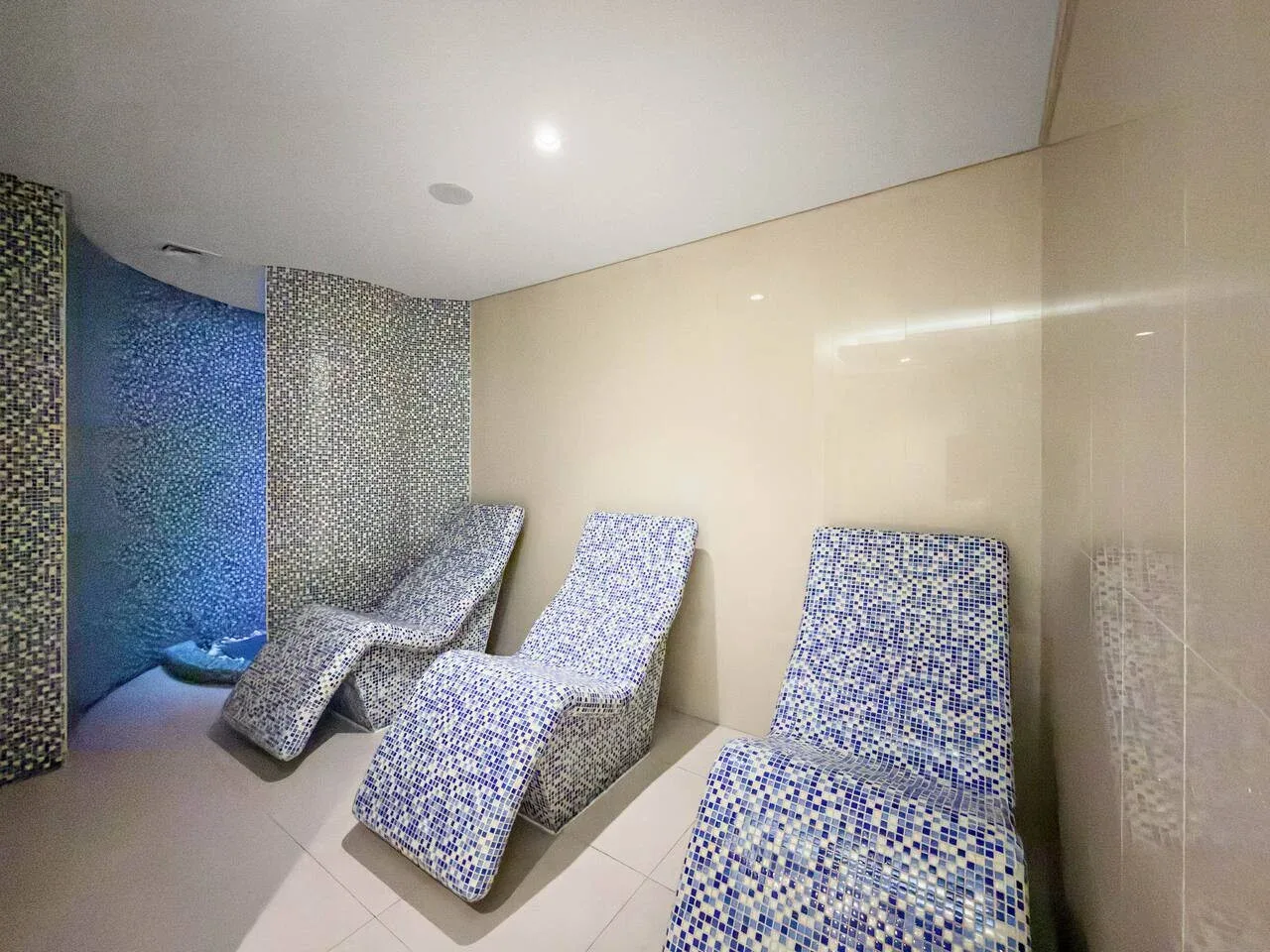 A tiled relaxation room with several reclining seats beside a blue-lit wall.