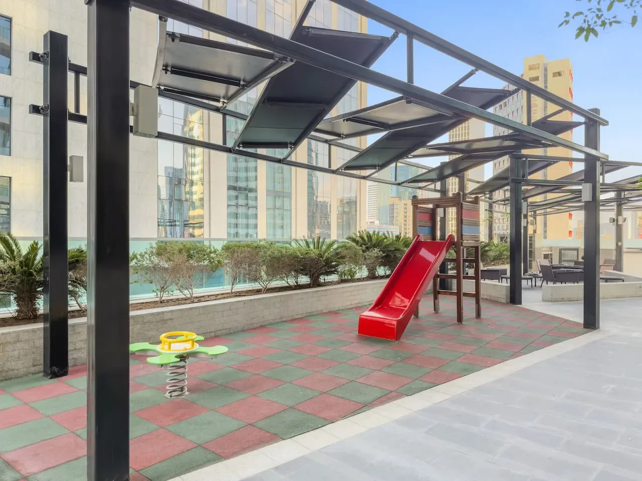 An outdoor play area with a red slide beneath a metal canopy.
