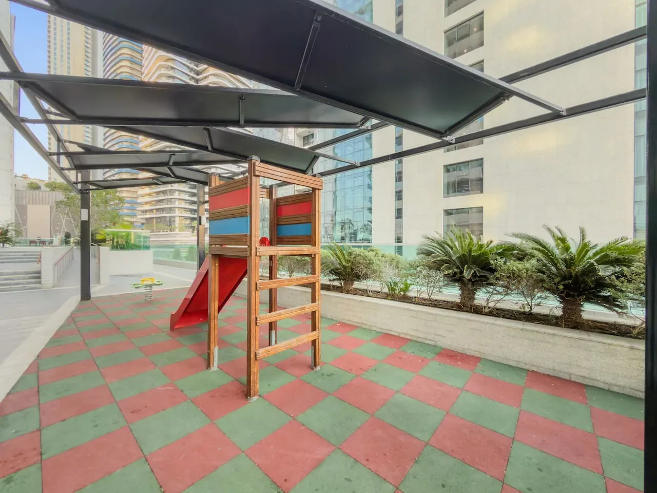 A covered outdoor playground with a small wooden climbing structure on a tiled surface.