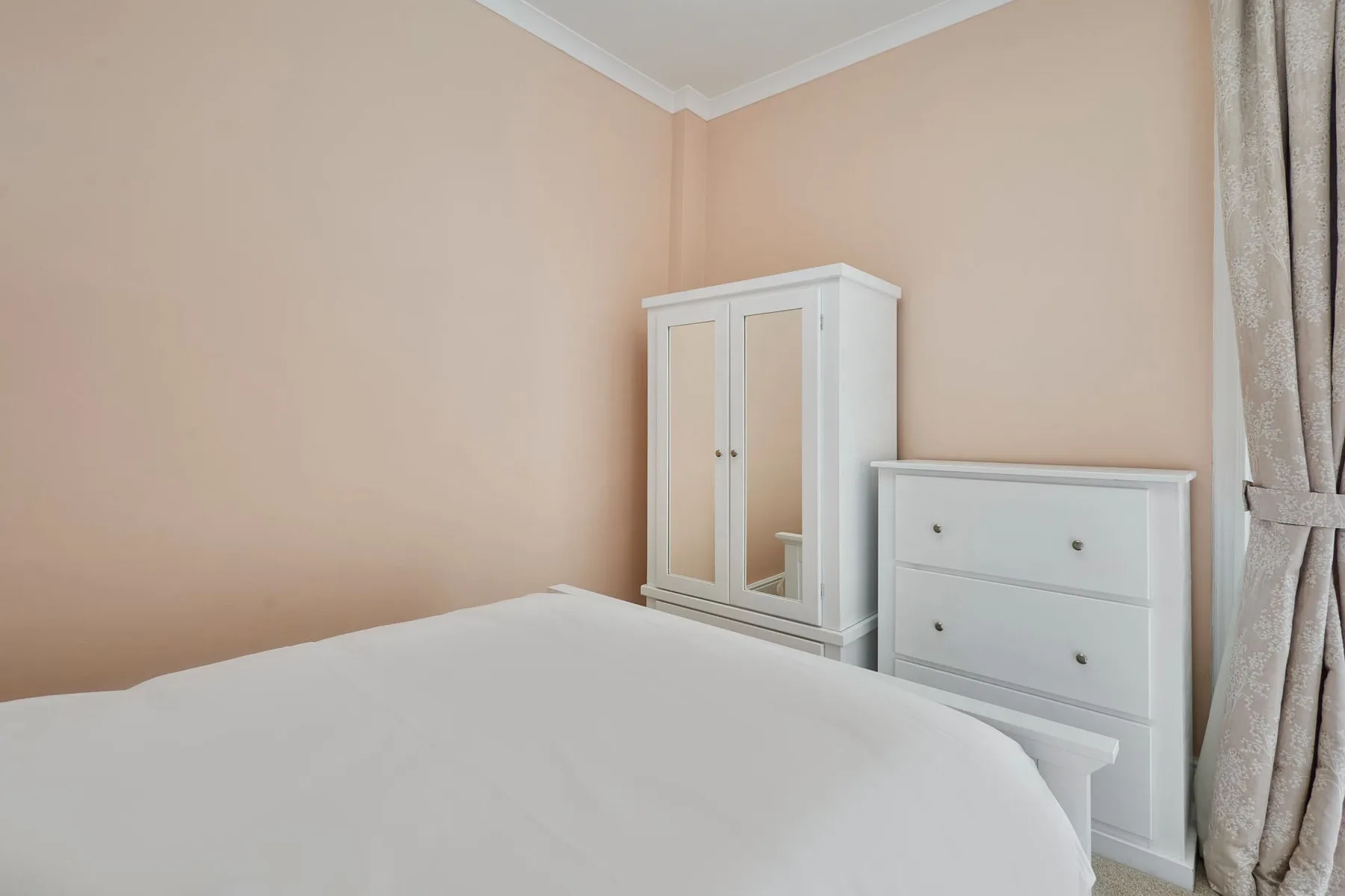 Bedroom with a white bed, wardrobe, and chest of drawers.