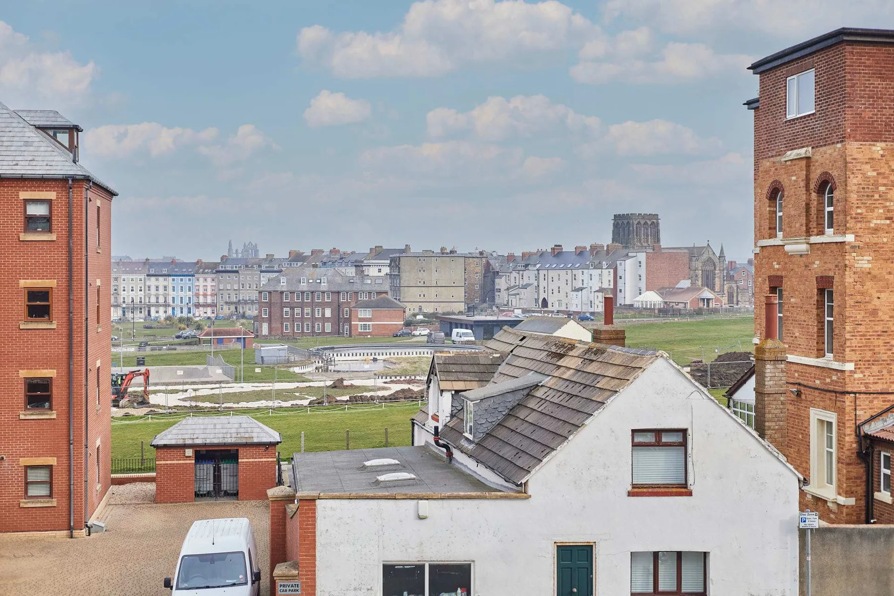 An urban neighborhood with brick buildings, rooftops, and a green open area.