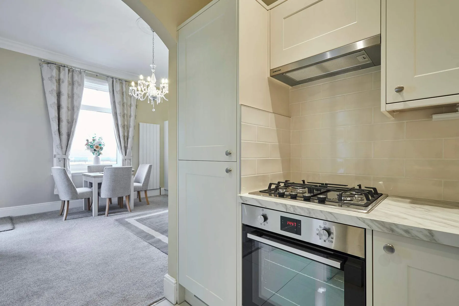 A bright kitchen opens onto a dining area with a table and chairs.
