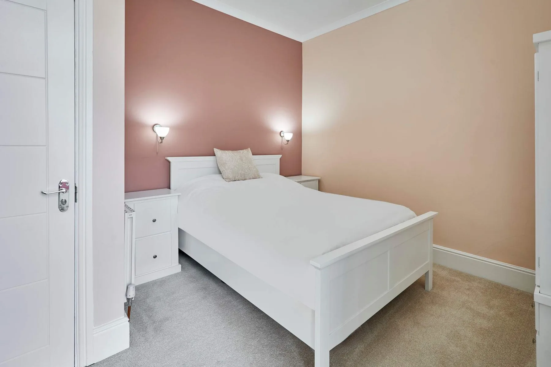 A bedroom with a white bed against a pink accent wall.