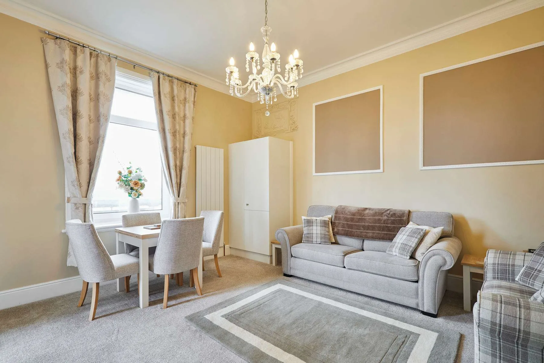 A bright living room with a gray sofa, dining table, and large window.