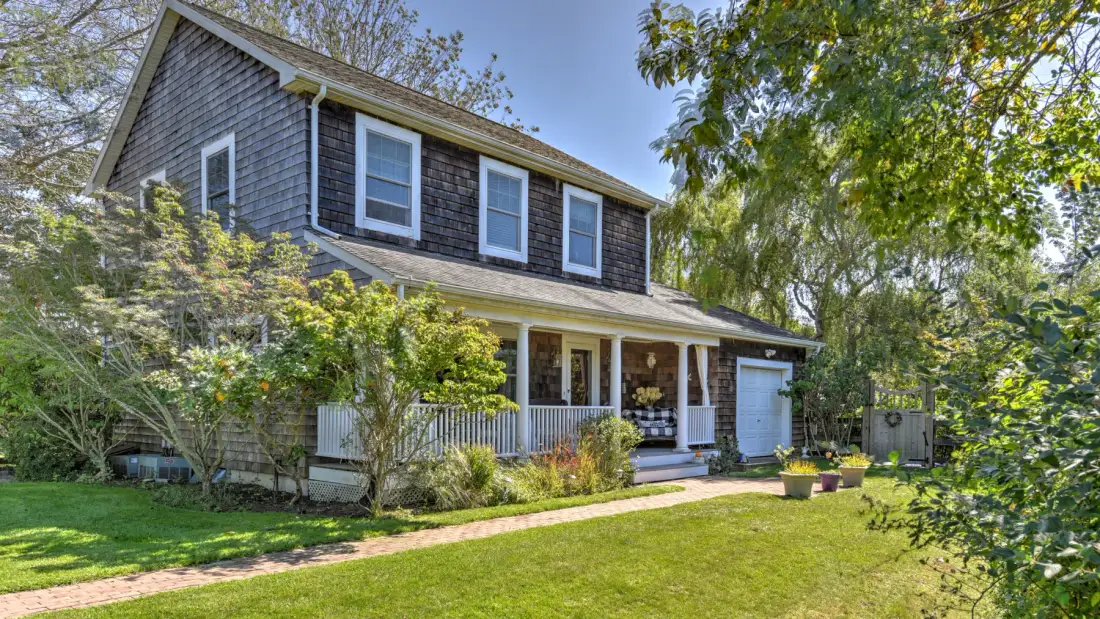 A two-story house with a covered porch stands behind a green lawn.