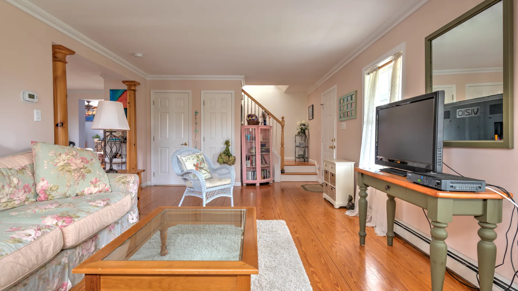 A living room with floral seating, a glass coffee table, and a television.