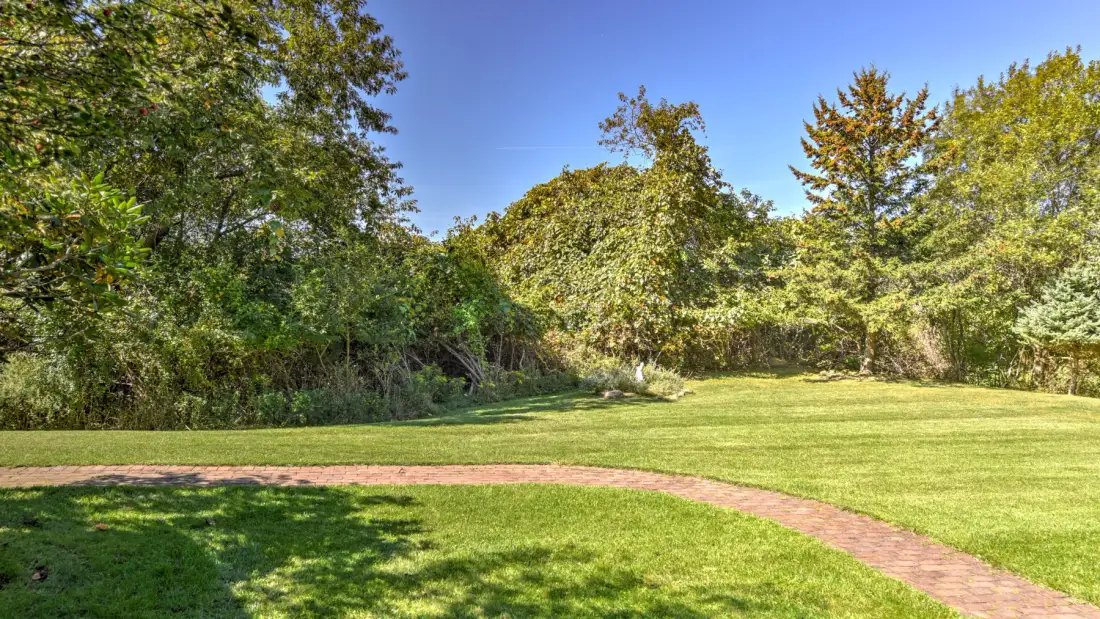 A grassy clearing bordered by trees, with a curving brick path.