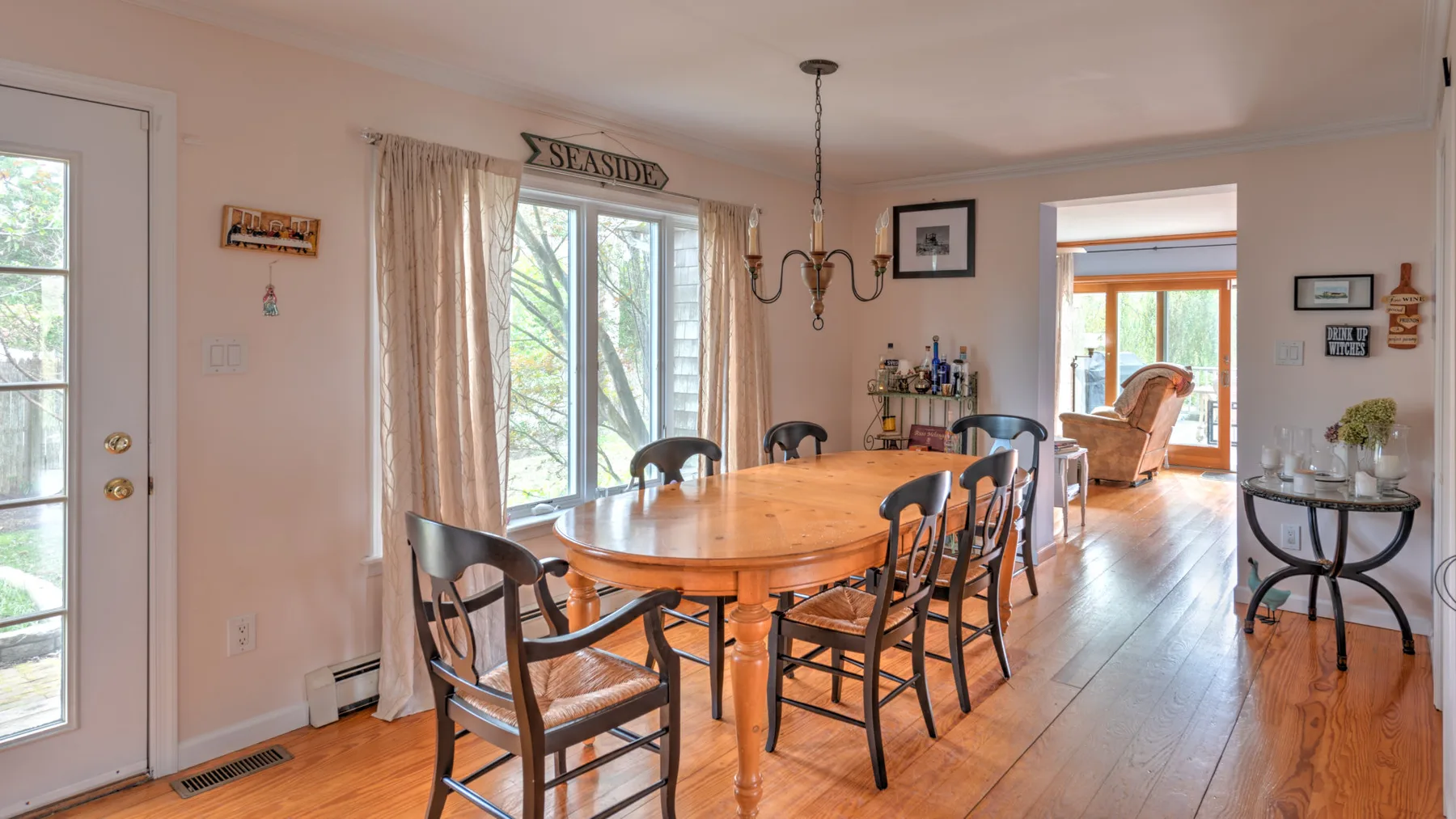 A dining room with a wooden table and chairs beside large windows.