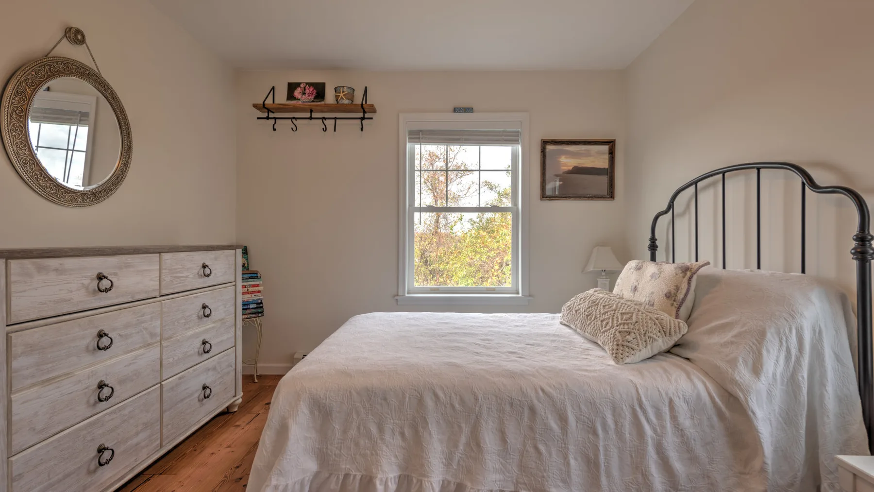 A bedroom with a bed, dresser, and window overlooking trees.