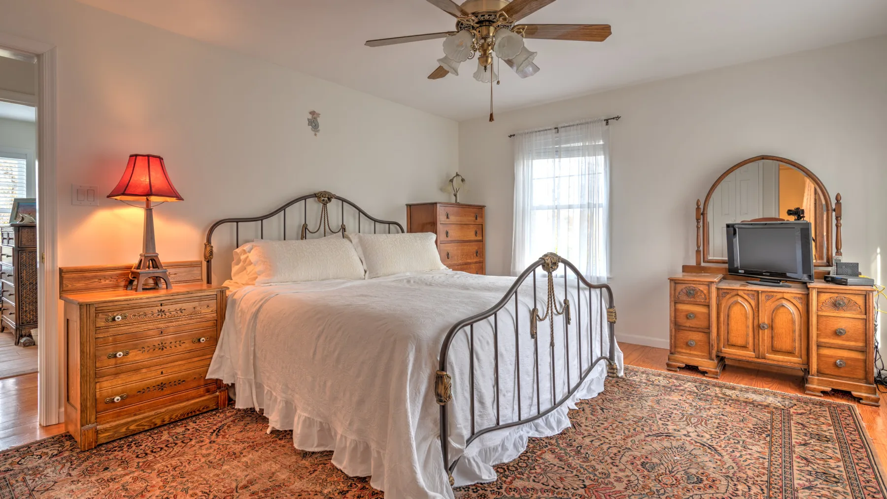 A bedroom with a metal bed, wooden dressers, and a patterned rug.