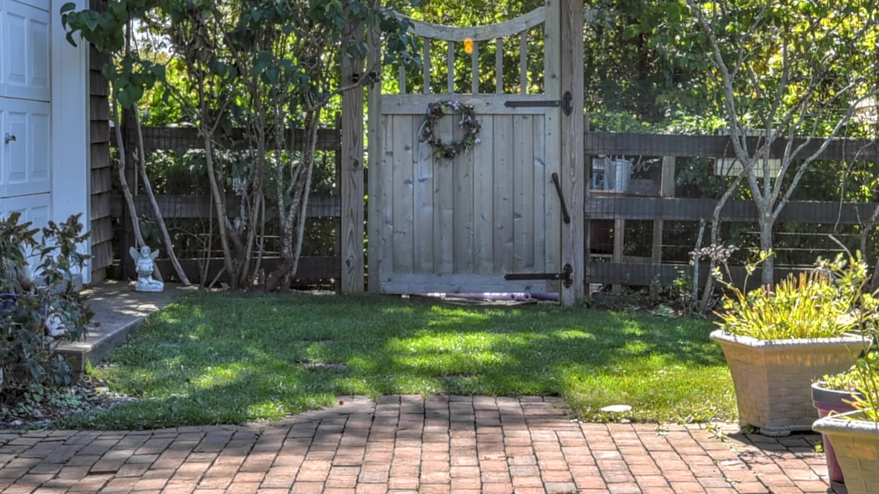 A garden patio with a brick walkway, lawn, and wooden gate.