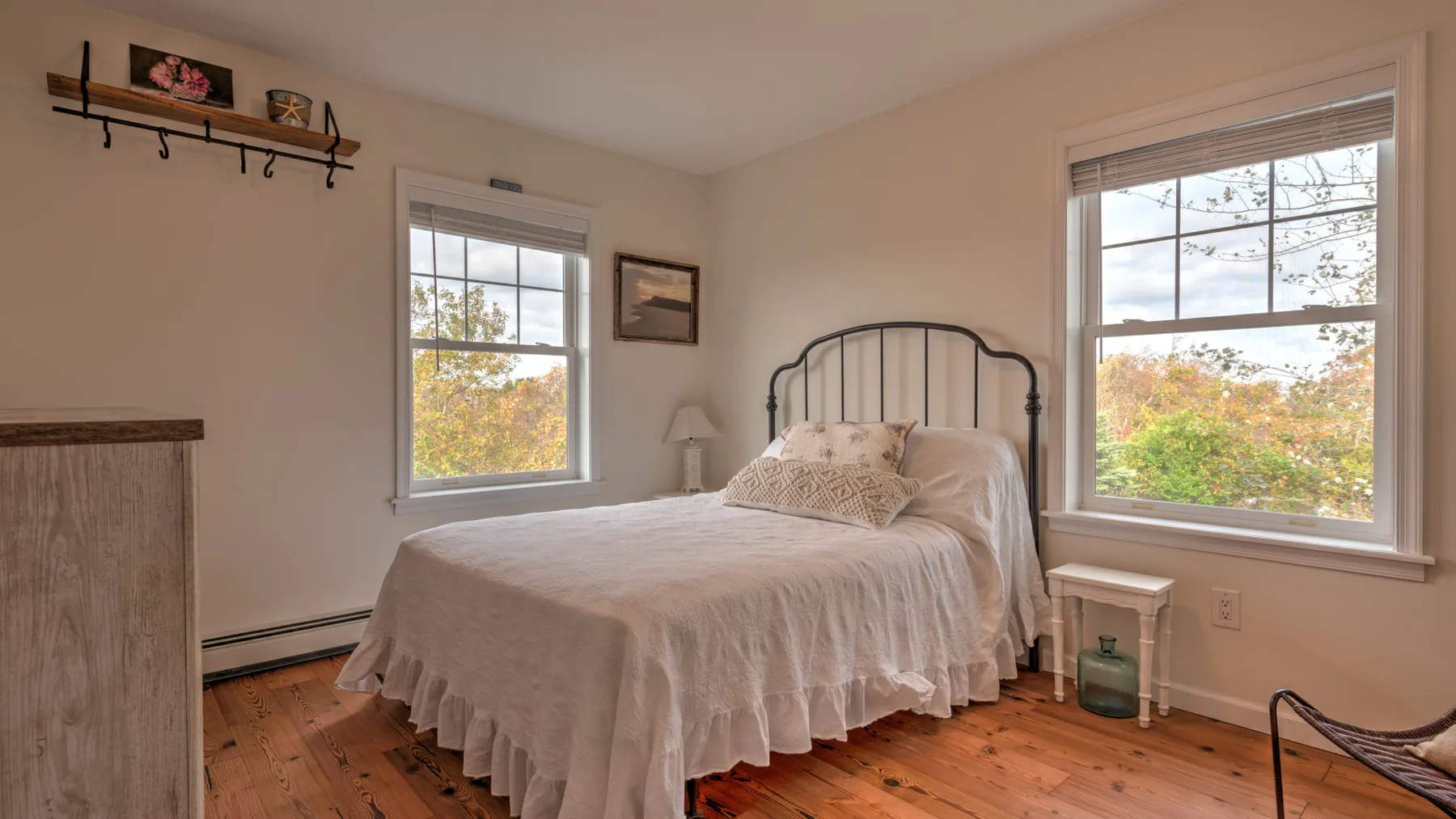 A bedroom with a bed between two windows overlooking leafy trees.