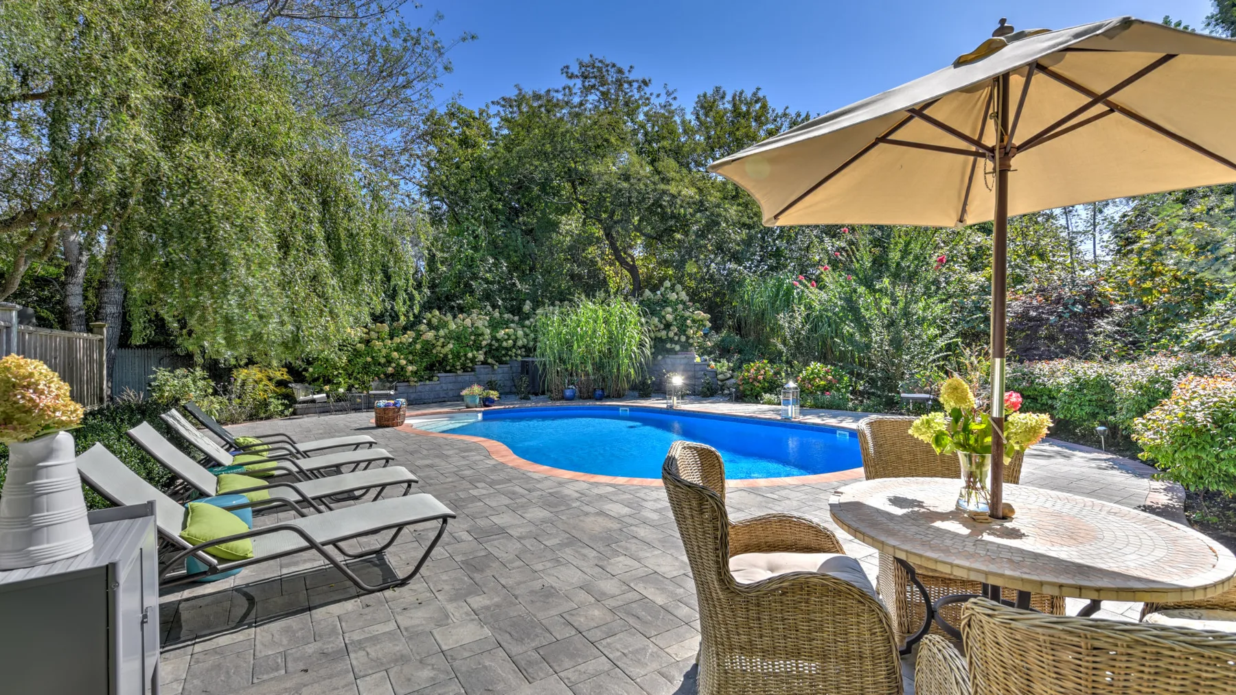 A swimming pool and patio seating sit among leafy trees.