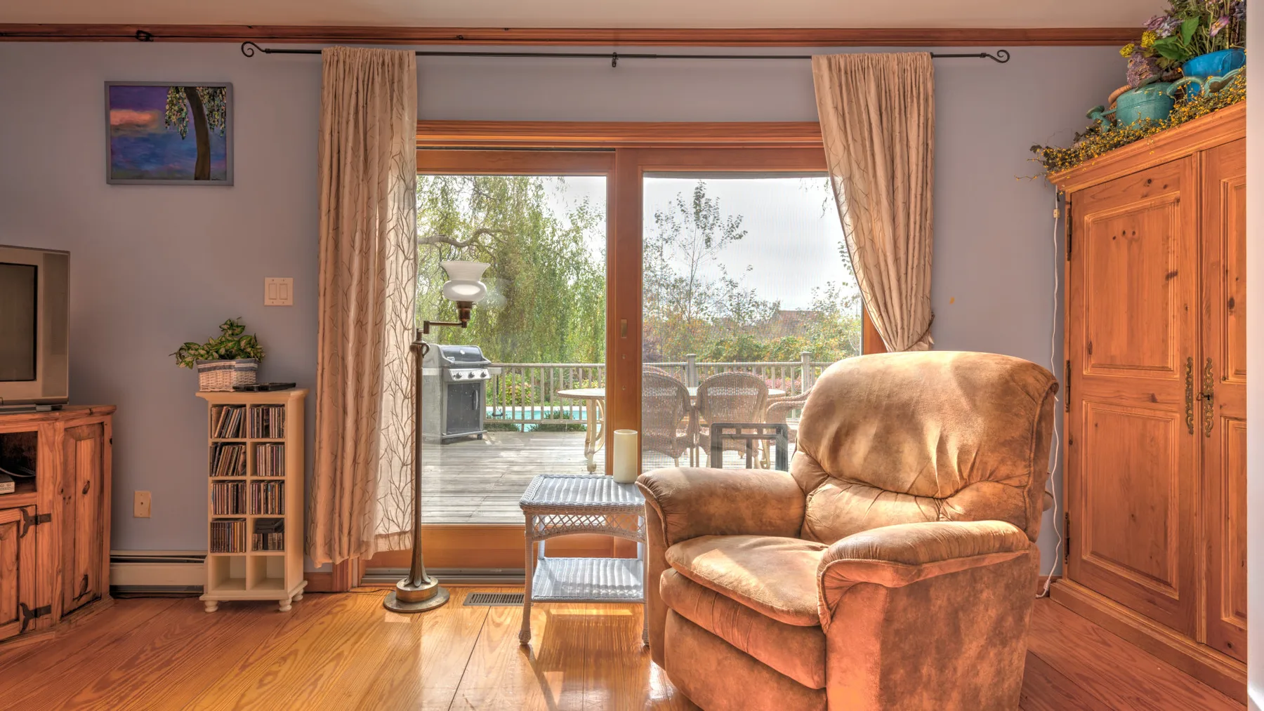 A living room with a cushioned armchair beside glass doors opening onto a deck.