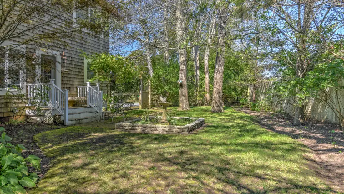 A leafy backyard with a raised garden bed beside a house.