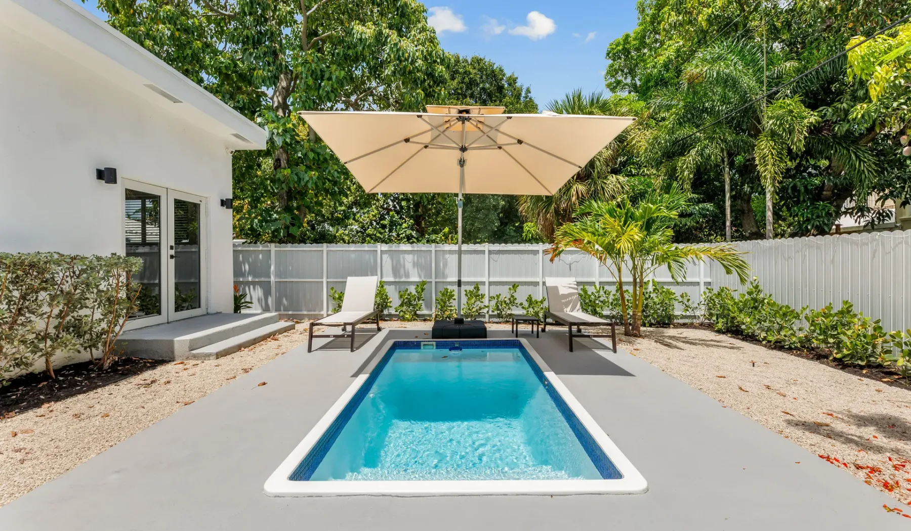 Una piscina en el patio está junto a una terraza con asientos y una sombrilla.