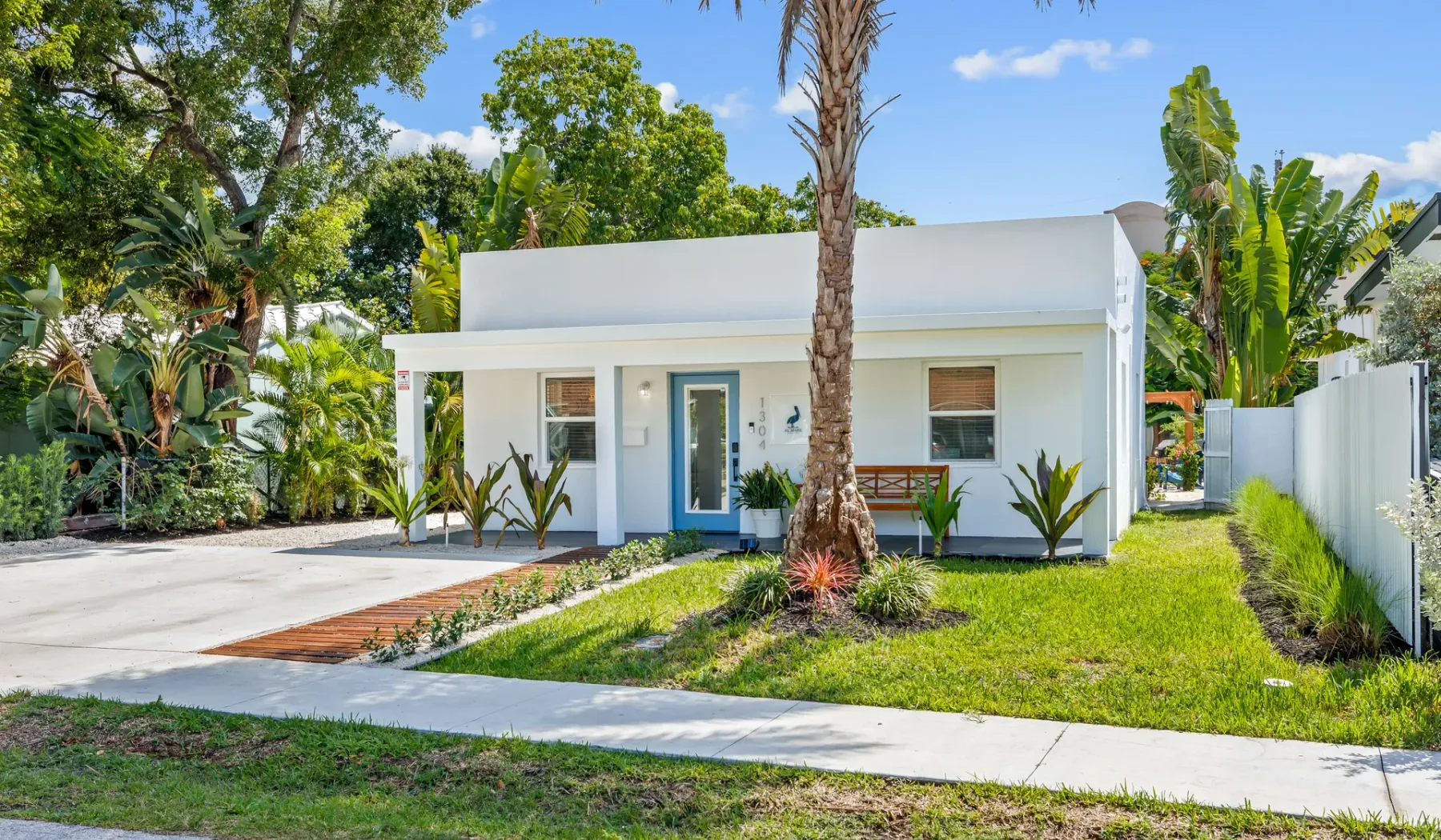 Una casa moderna de una planta está rodeada de césped y plantas tropicales.