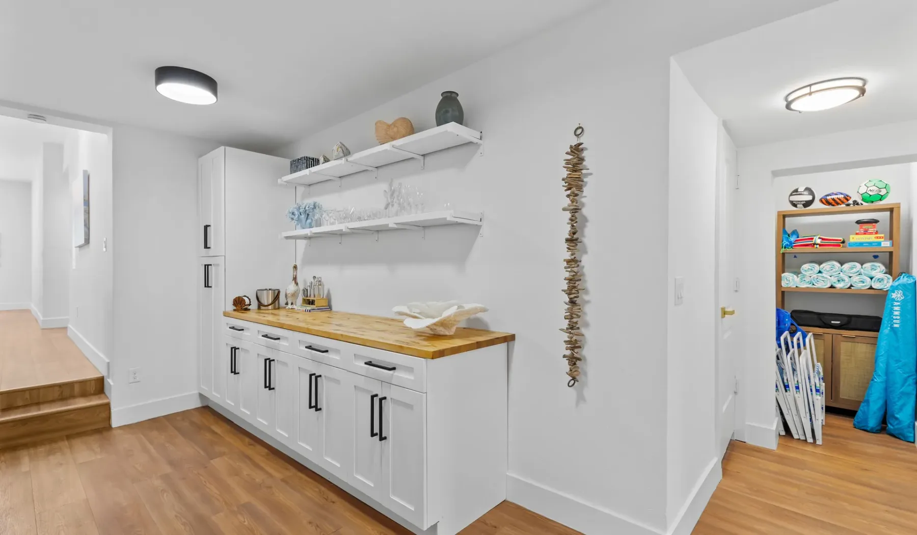Un pasillo luminoso con armarios blancos y una encimera de madera junto a una zona de almacenamiento abierta.