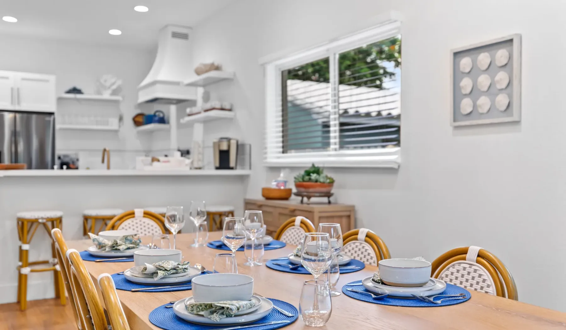 Una mesa está puesta en una cocina luminosa, con gabinetes blancos y una ventana.
