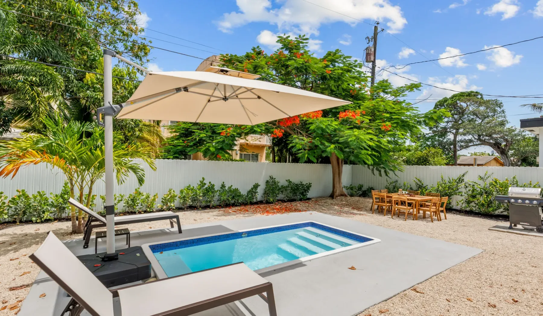 Una piscina al aire libre y un patio con una gran sombrilla y una mesa de comedor cercana.
