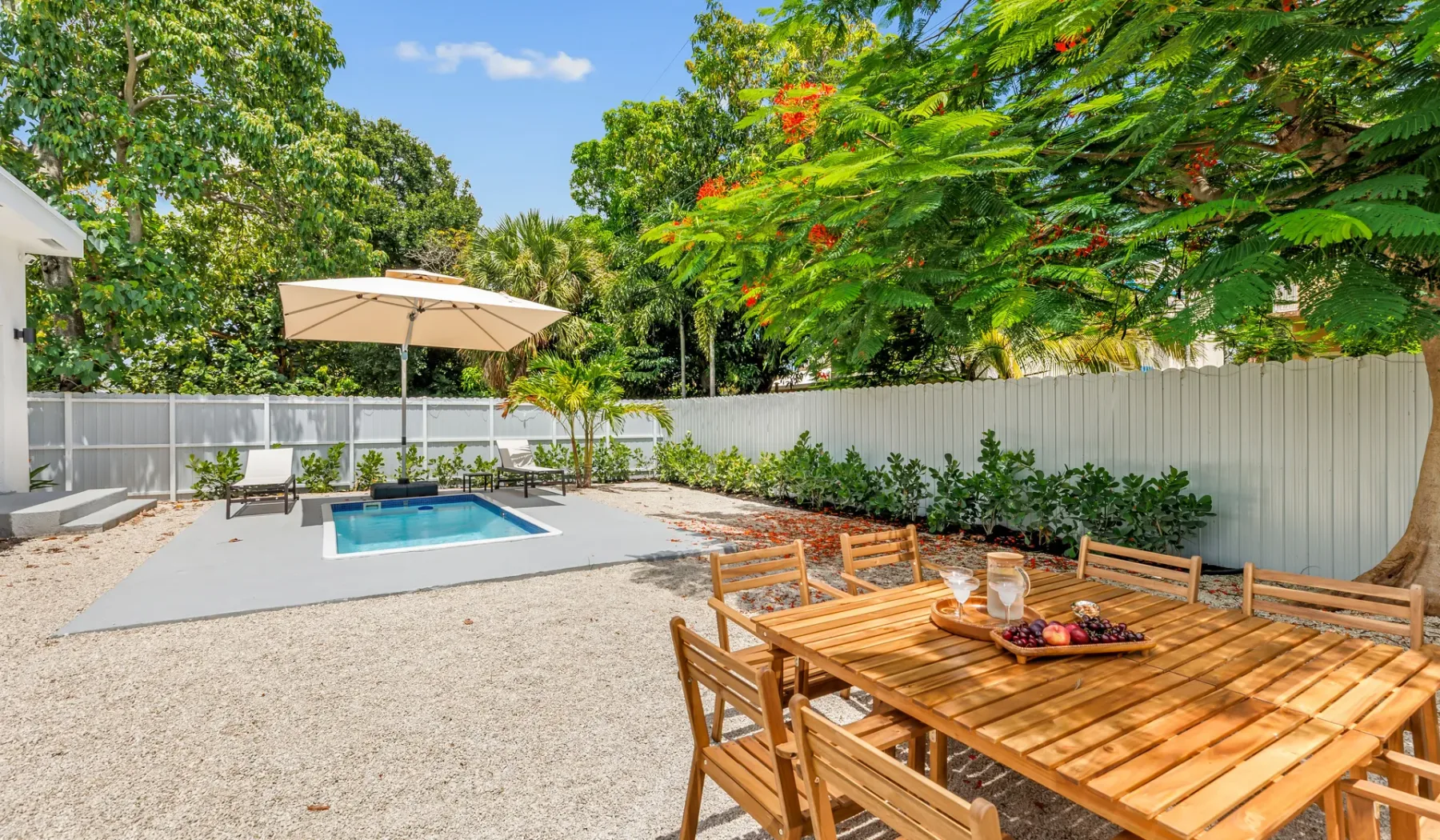 Un patio exterior con una mesa de comedor de madera junto a una pequeña piscina.
