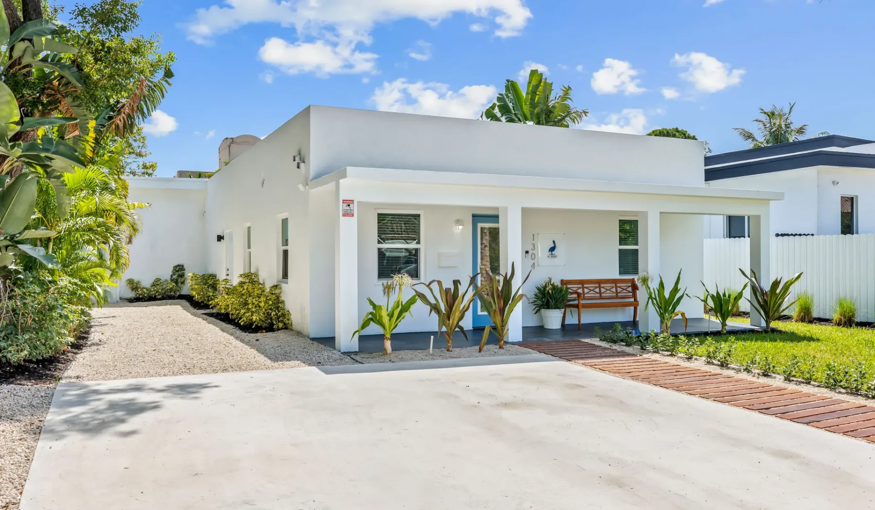 Exterior de una casa blanca moderna con una entrada amplia y plantas frondosas.