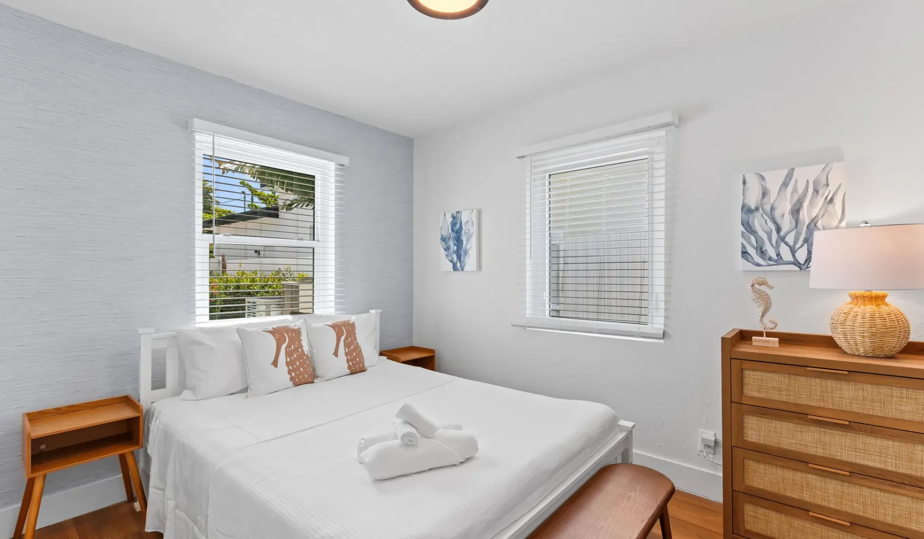 Un dormitorio con una cama blanca, ventanas y una cómoda de madera.