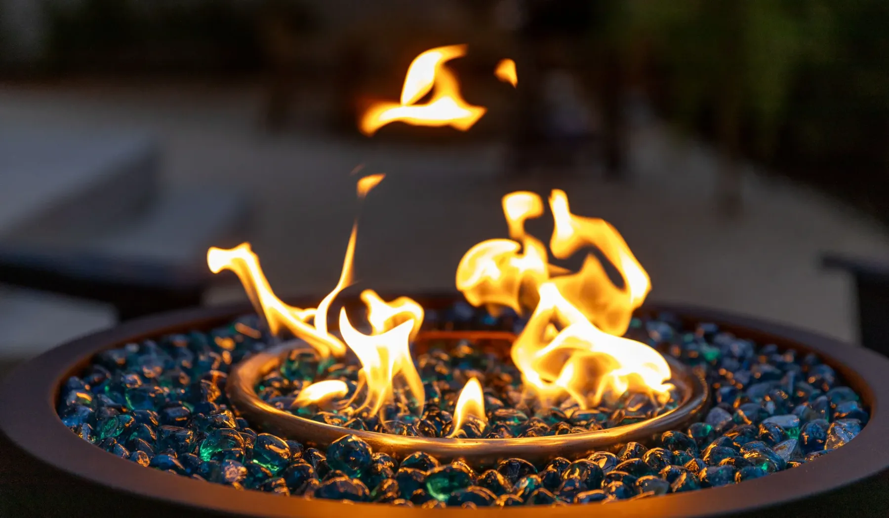 Un brasero circular al aire libre arde con llamas brillantes entre piedras oscuras.