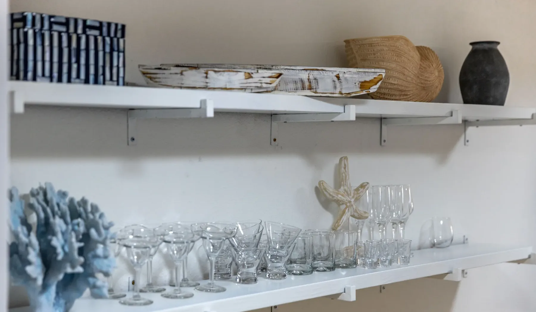 Una repisa de exhibición sostiene cristalería y objetos decorativos junto a una pared blanca.
