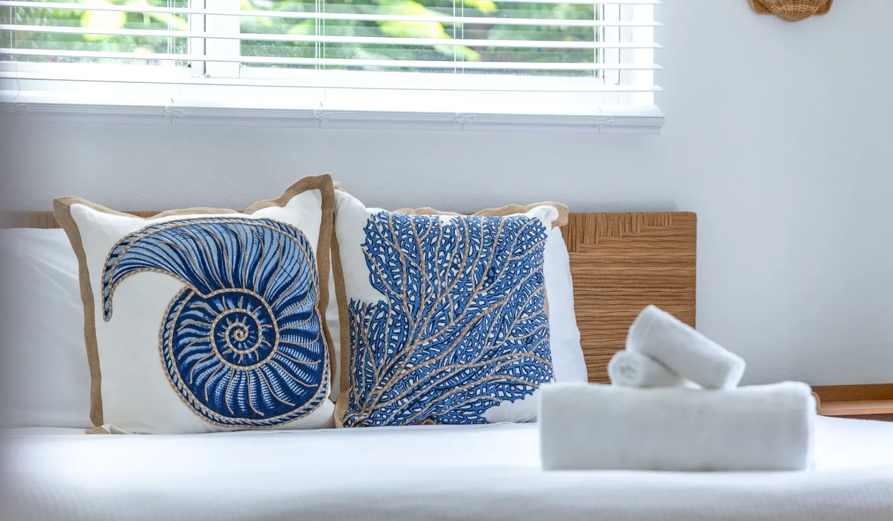 Una cama bien tendida con cojines azules estampados bajo una ventana.