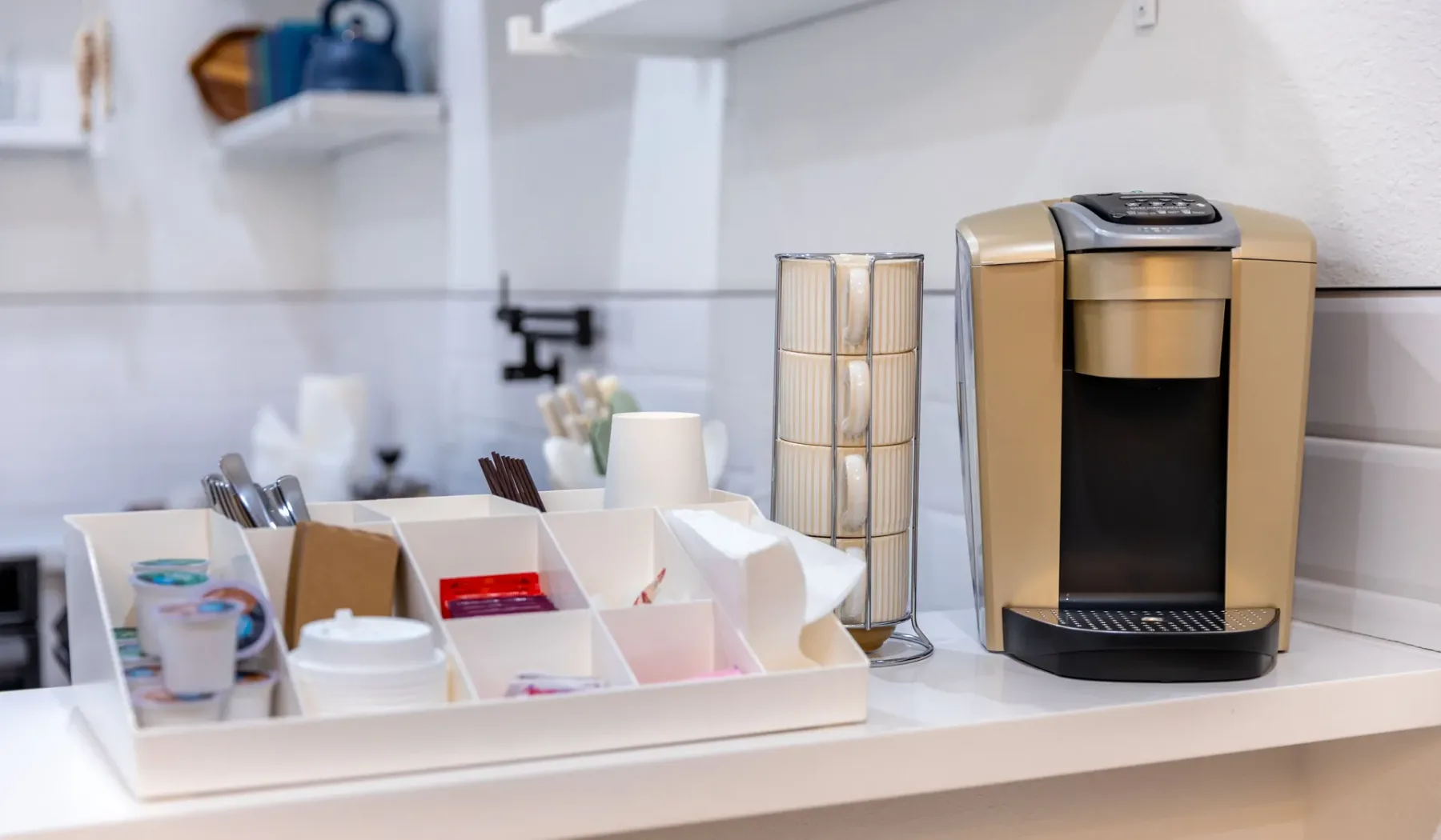 Una estación de café con una cafetera y tazas y suministros organizados.