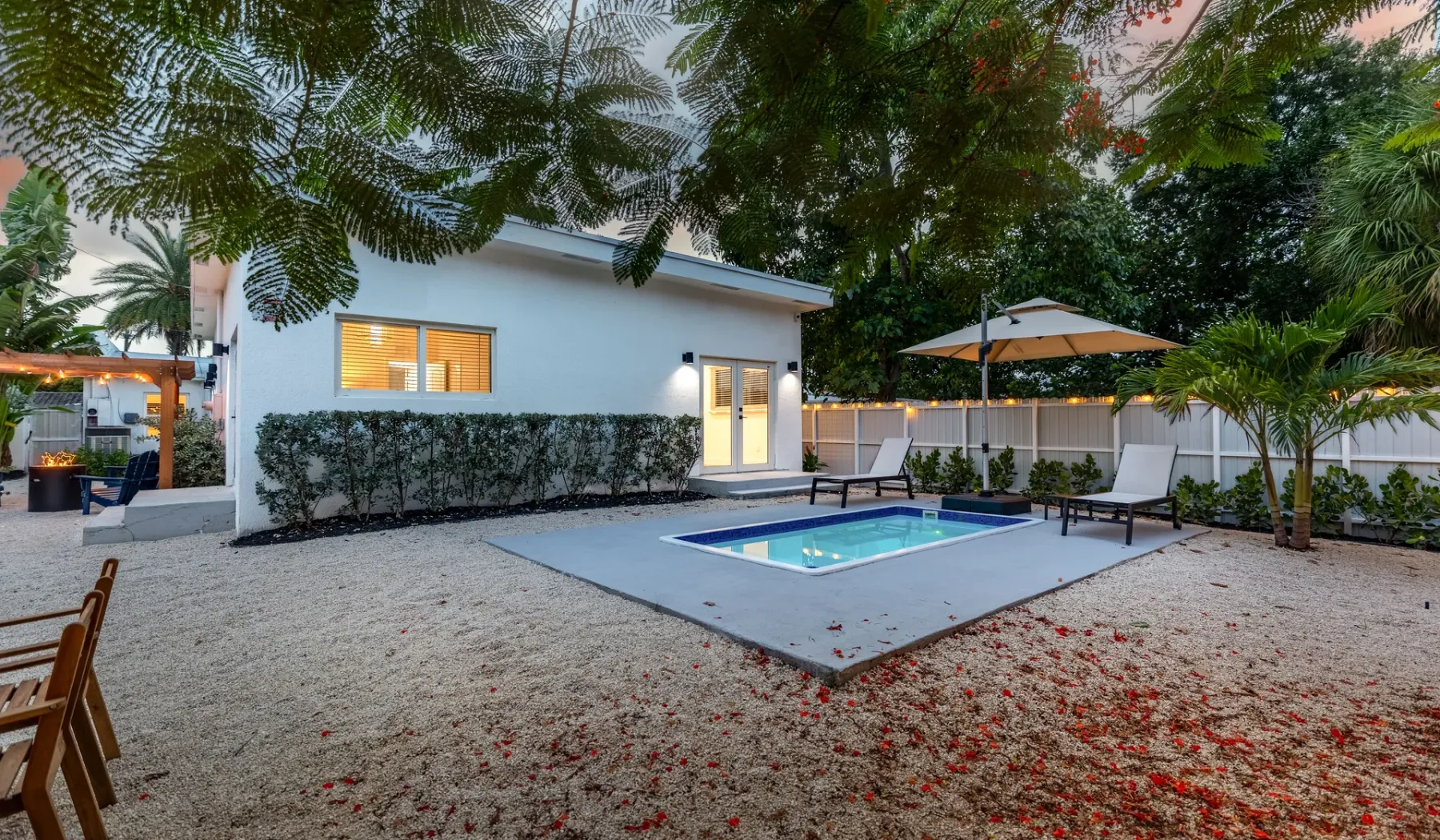 Un patio trasero con una piscina pequeña, tumbonas y árboles.