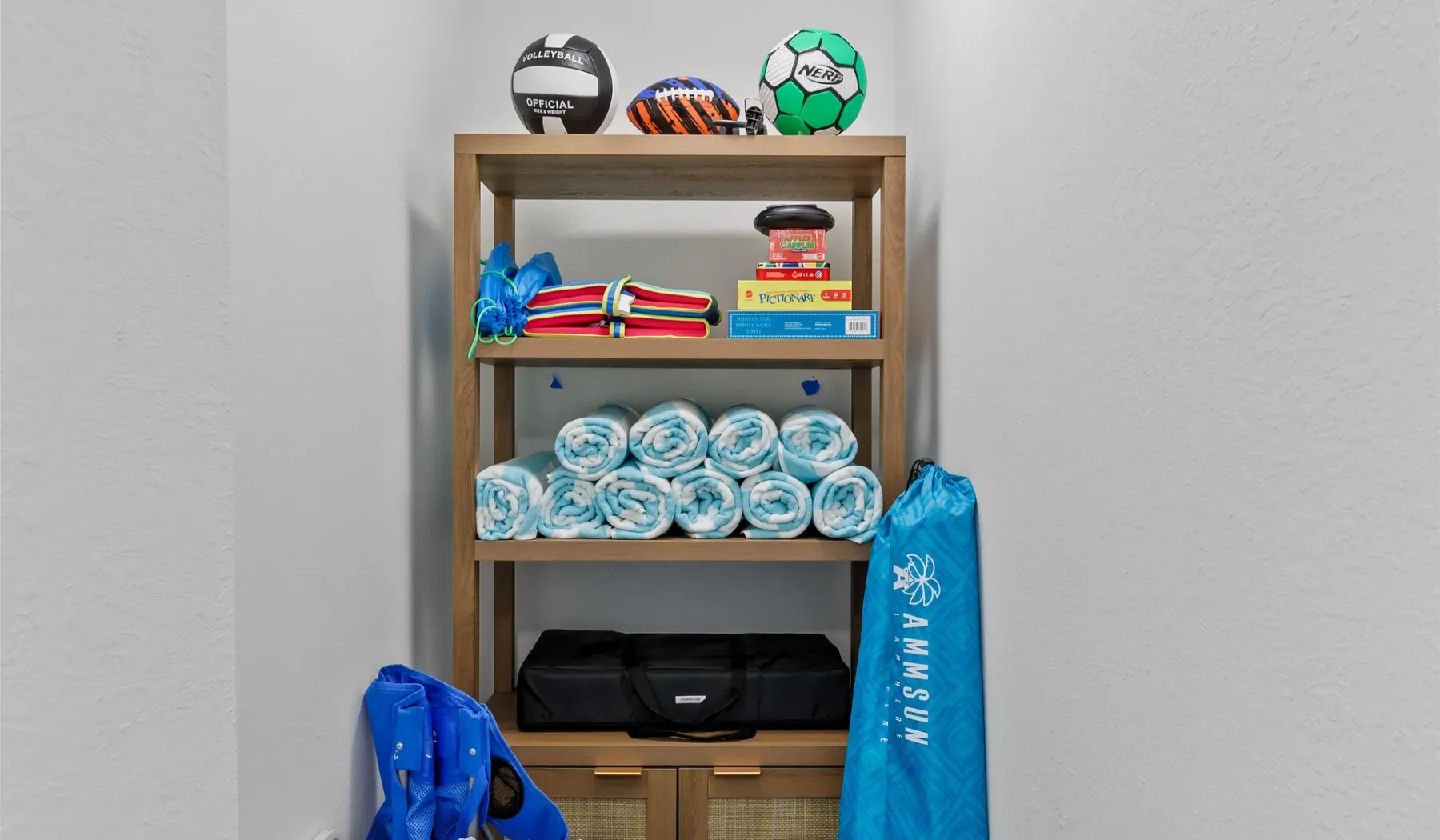 Una estantería de madera muestra balones deportivos, toallas dobladas y una bolsa azul.