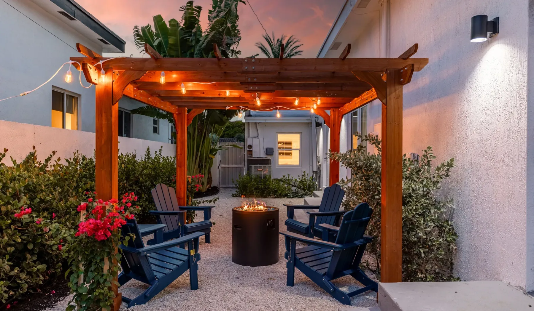 Un patio al aire libre con asientos alrededor de una fogata bajo una pérgola de madera.