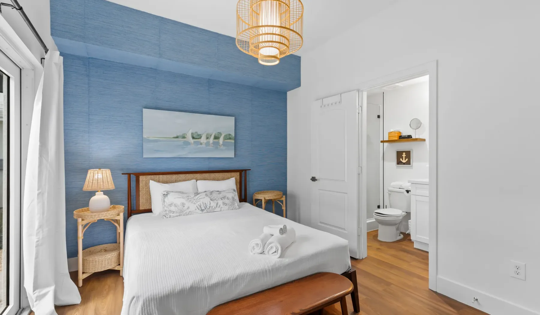 Un dormitorio luminoso con una cama blanca, una pared azul y la puerta del baño abierta.