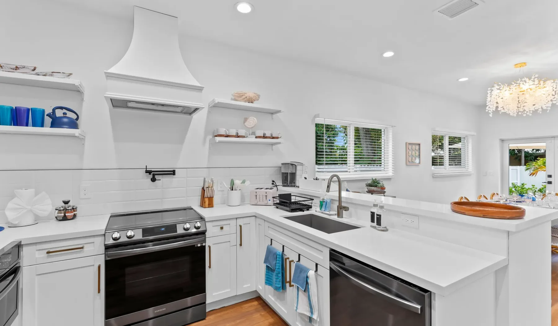 Una cocina blanca y luminosa con isla, electrodomésticos de acero inoxidable y ventanas.