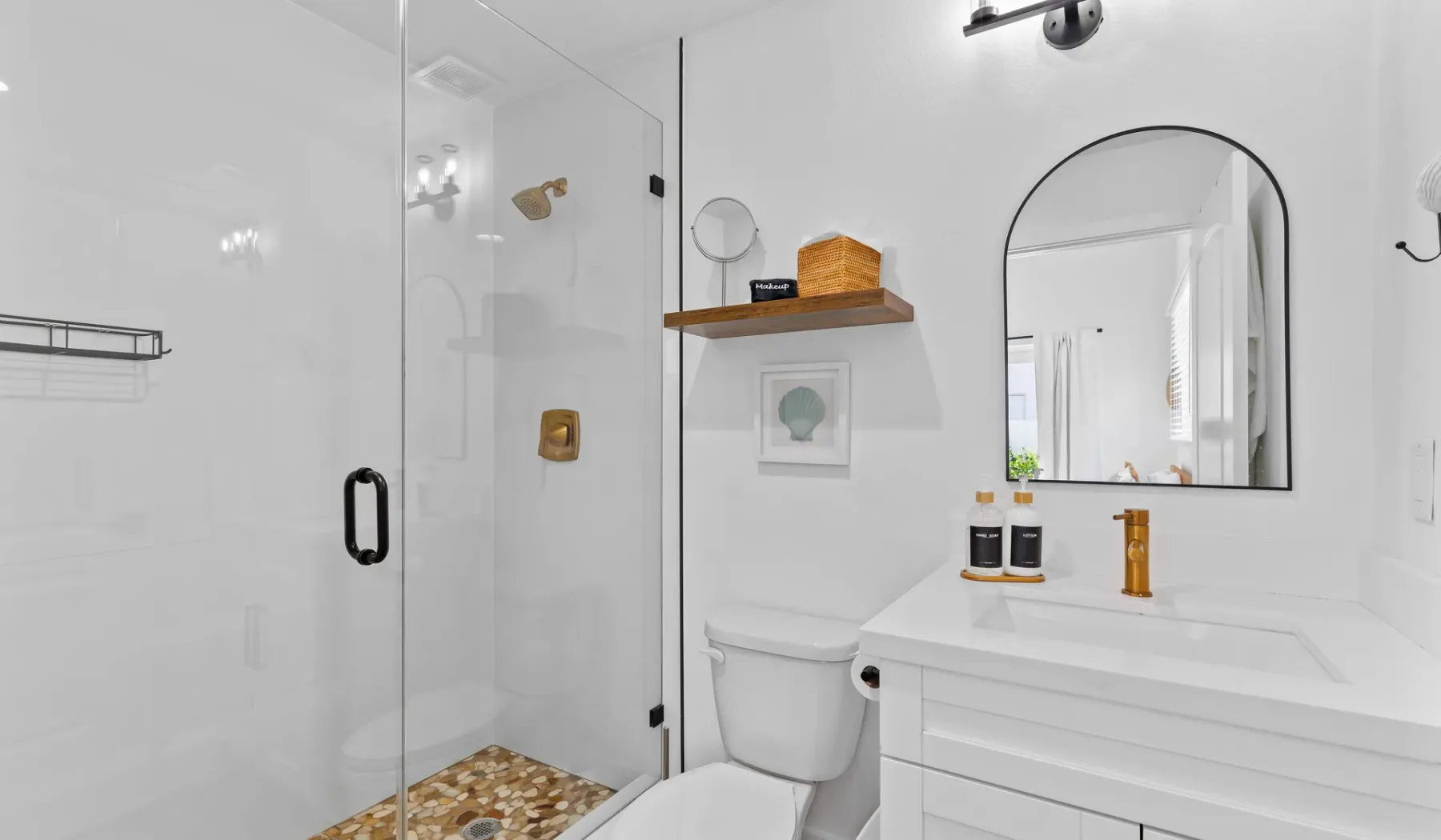 Un baño luminoso con una ducha de vidrio y un tocador bajo un espejo arqueado.