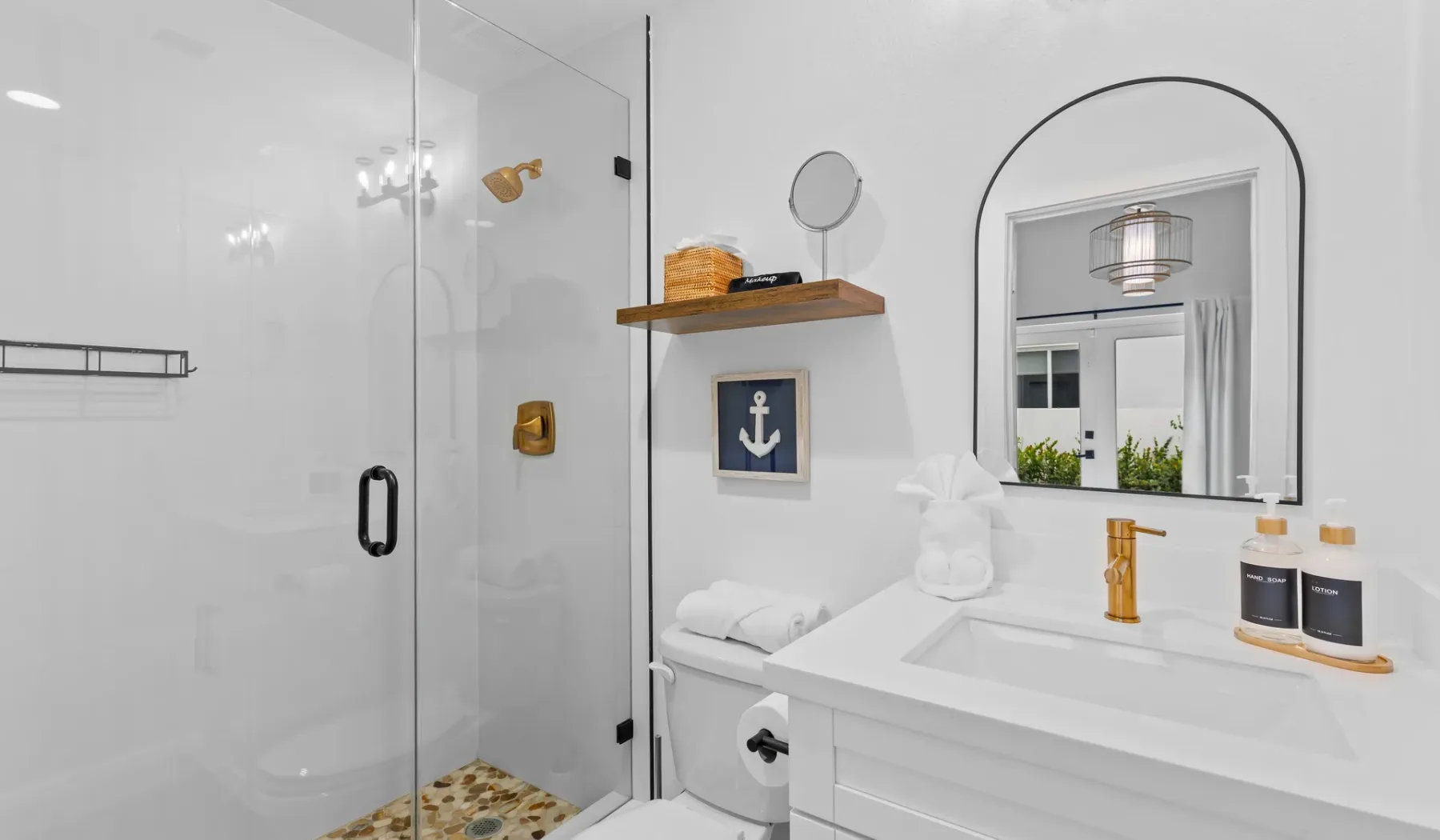 Un baño luminoso con una ducha de vidrio y un amplio lavabo bajo un espejo arqueado.