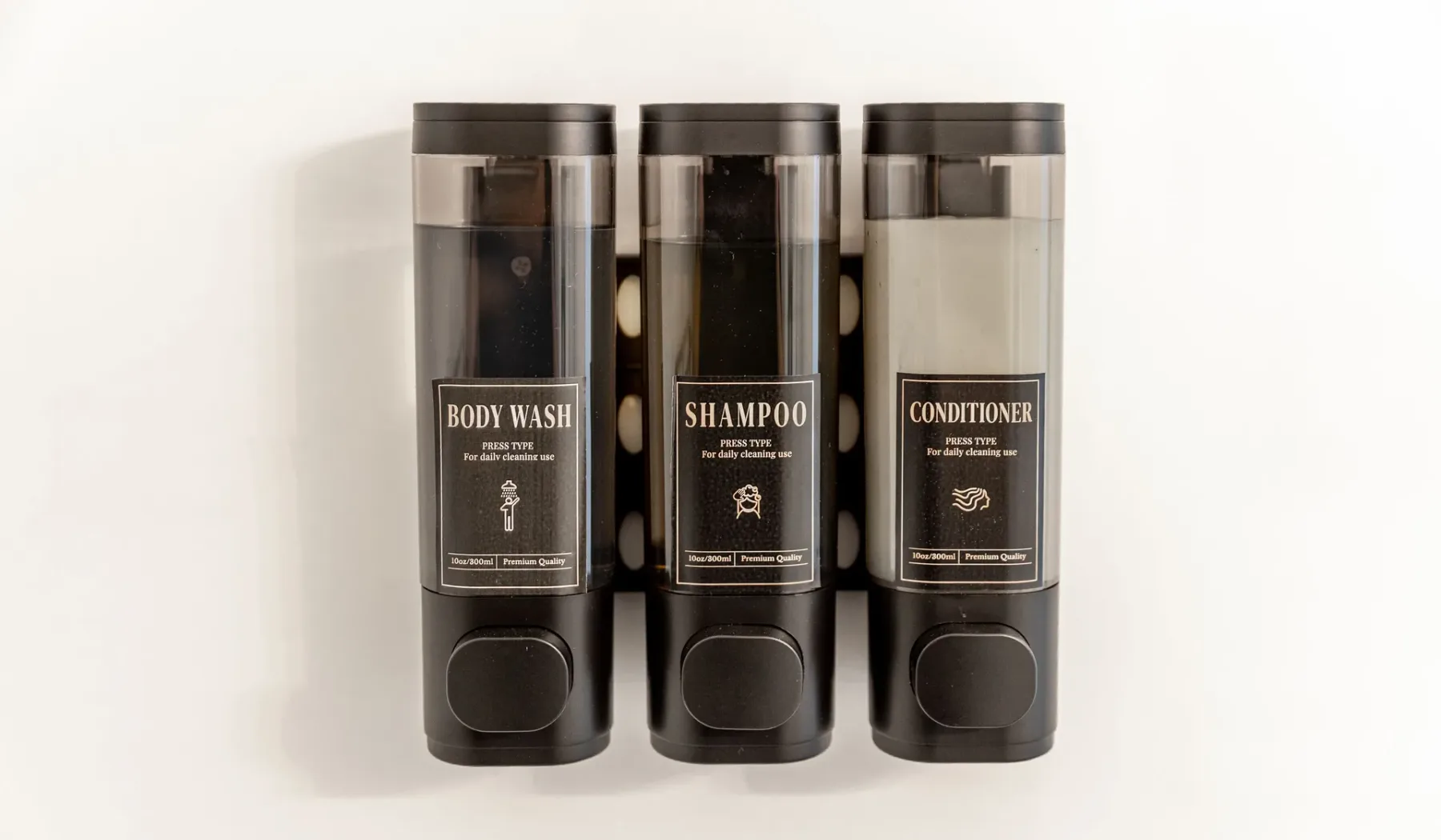 Tres dispensadores de pared etiquetados como gel de baño, champú y acondicionador.