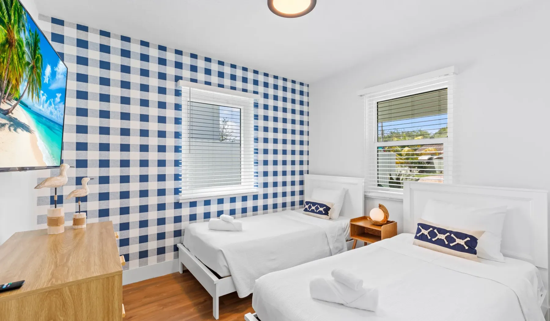 Un dormitorio luminoso con dos camas, paredes a cuadros azules y blancas, y ventanas.