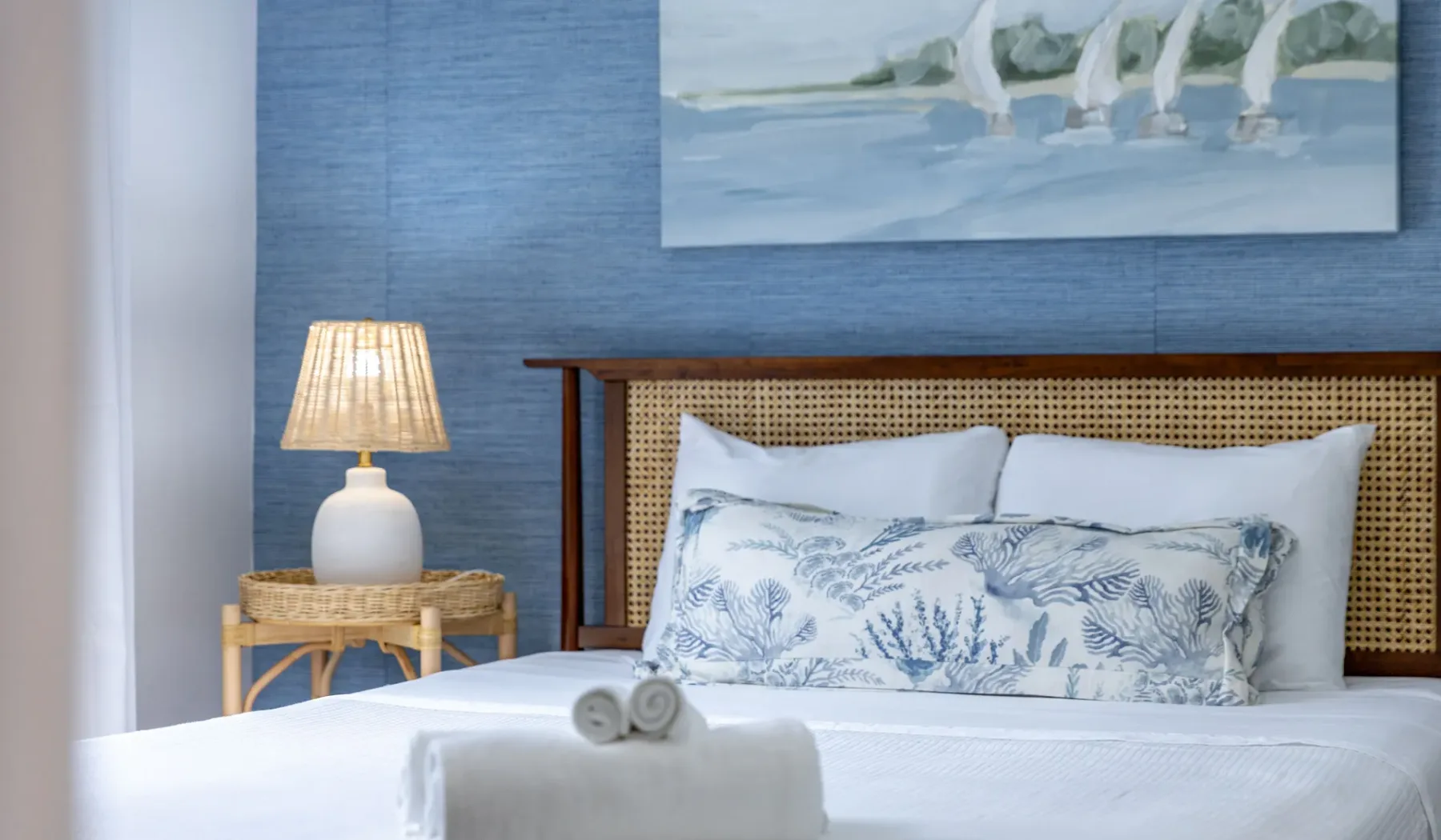 Una cama bien tendida con almohadas estampadas está frente a una pared azul.