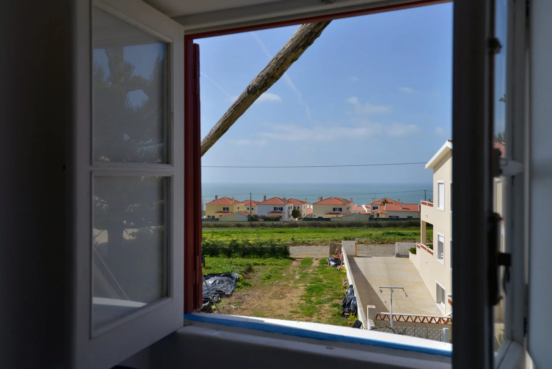 A window frames a view of nearby homes and the sea.