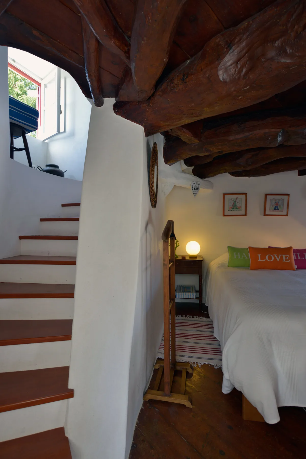 Dormitorio con una cama bajo vigas de madera vistas y una escalera al lado.