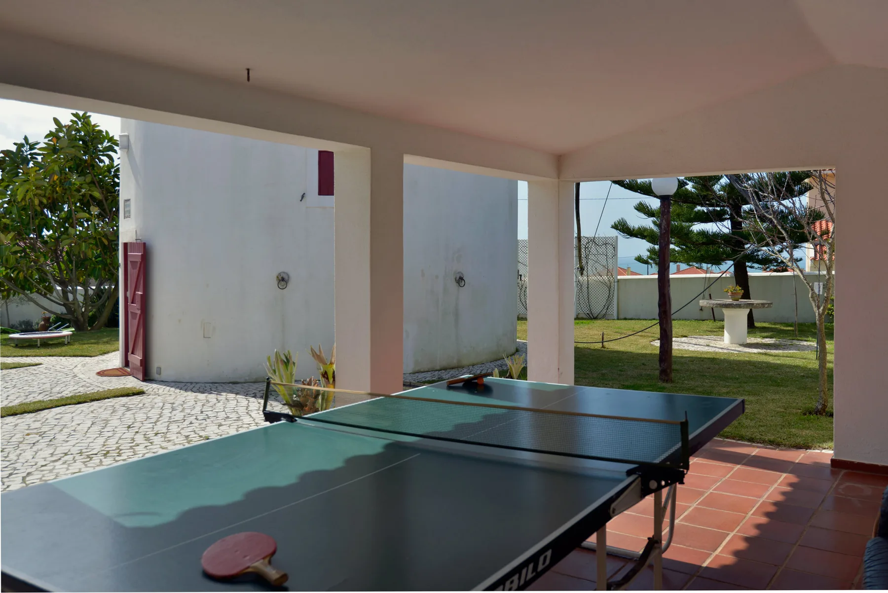 A covered outdoor table tennis area opens onto a garden.