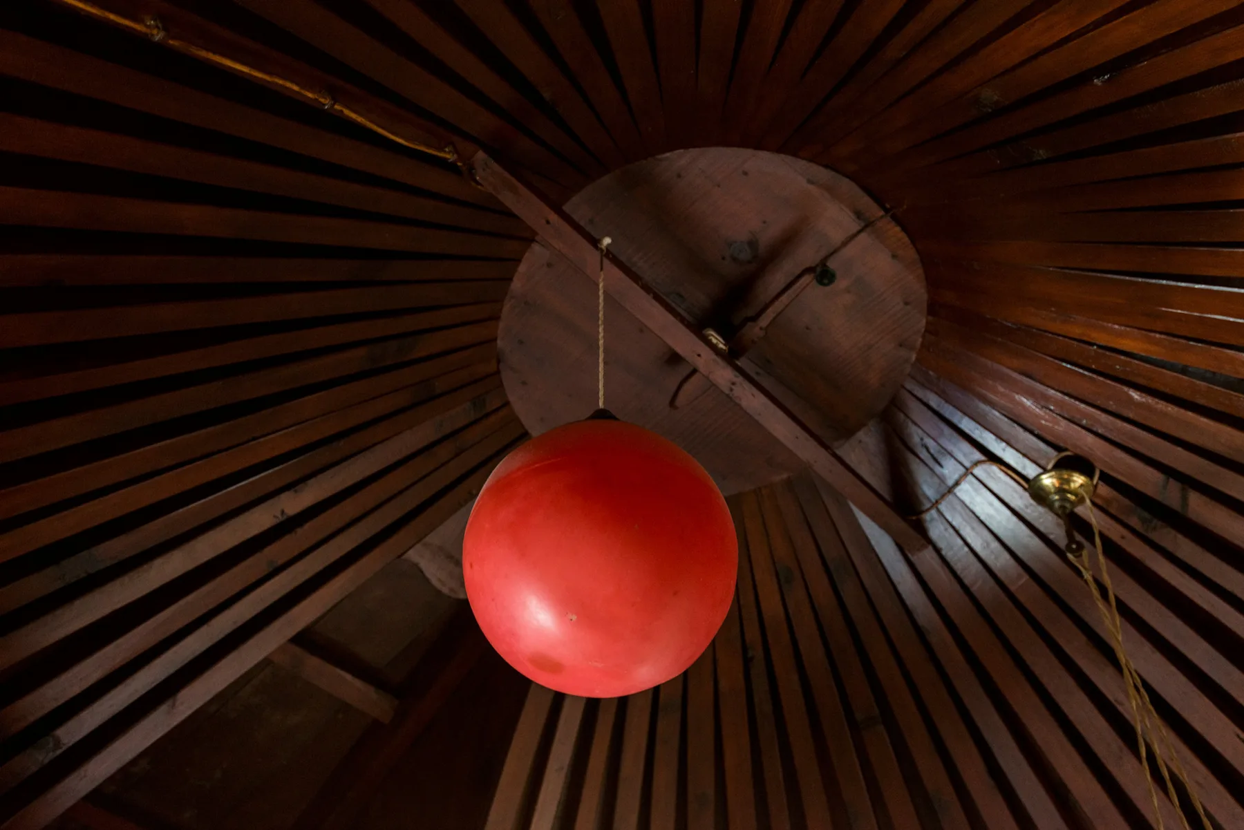 Un techo interior de madera con una lámpara colgante roja iluminada.
