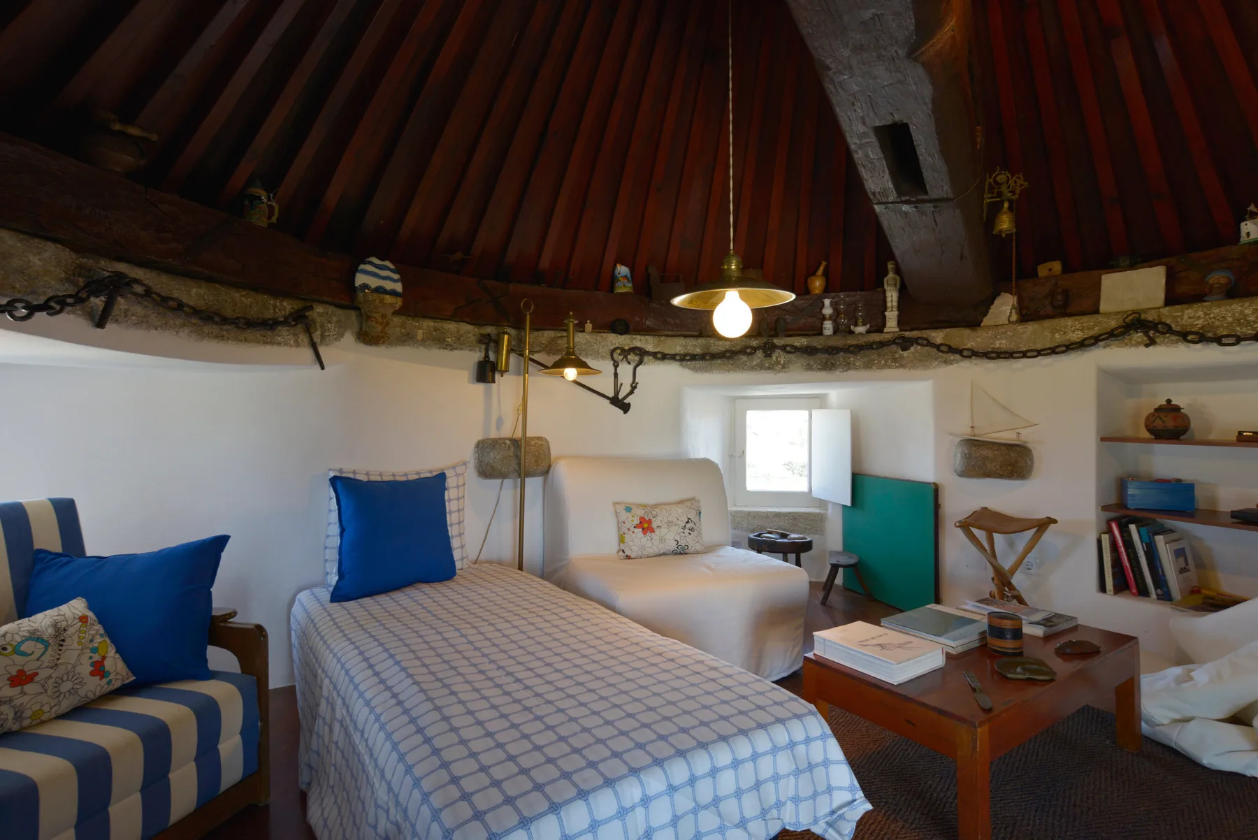 Un dormitorio con una cama, una zona de asientos a rayas y estantes bajo un techo inclinado de madera.