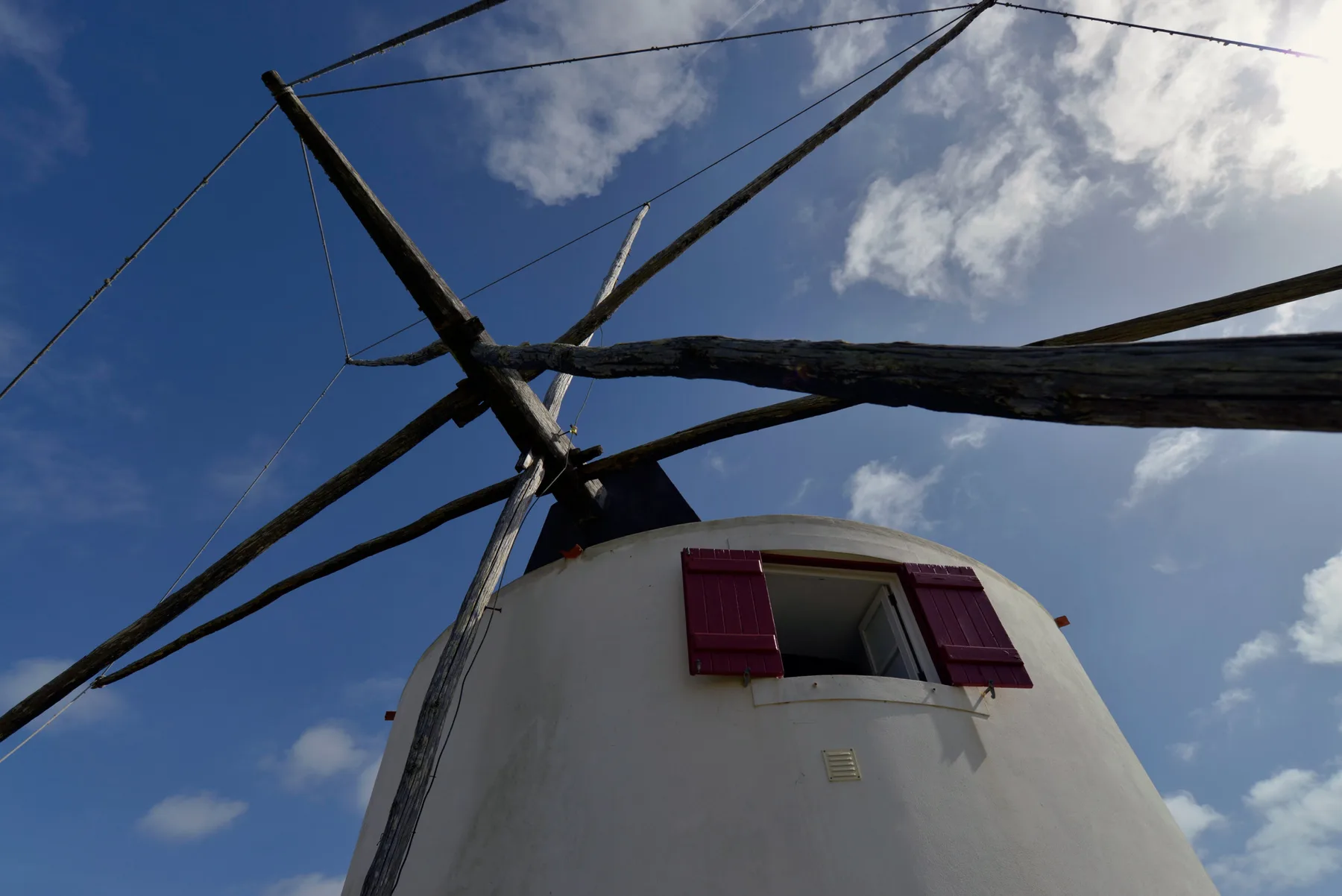Un molino blanco se alza bajo aspas de madera oscura y un cielo parcialmente nublado.
